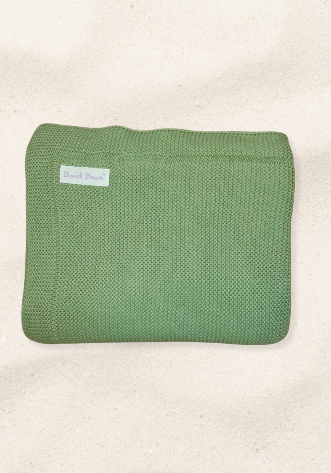 Folded green knitted baby blanket with a “Bondi Booti” label, placed on a light sandy background.