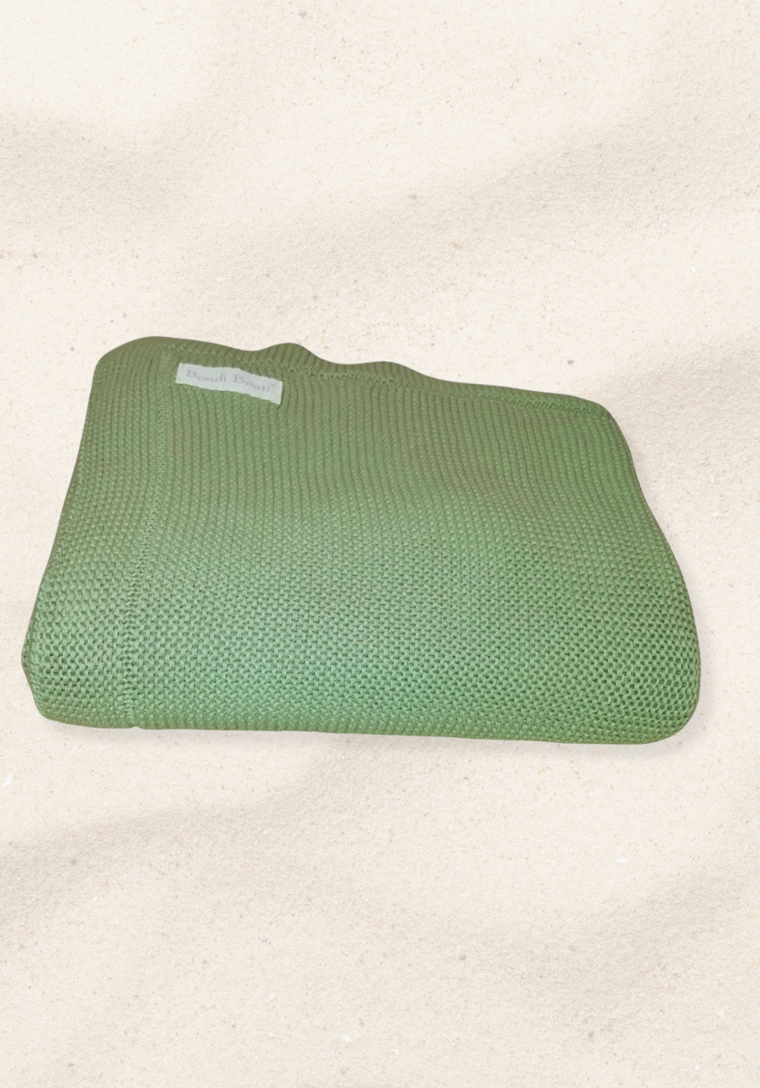 Folded green knitted baby blanket with a “Bondi Booti” label, placed on a light sandy background.