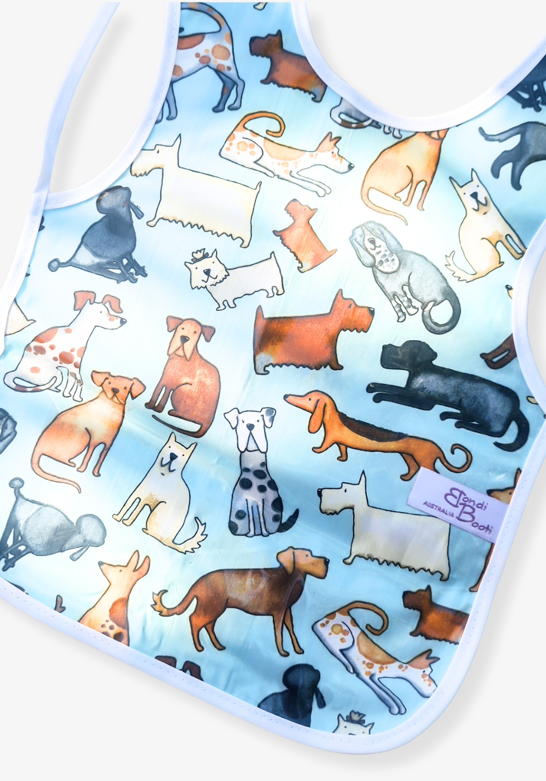 Laminated baby feeding bib featuring a playful pattern of illustrated dogs in various breeds and colors on a light blue background, trimmed in white with a snap closure, laid flat on a grey background.
