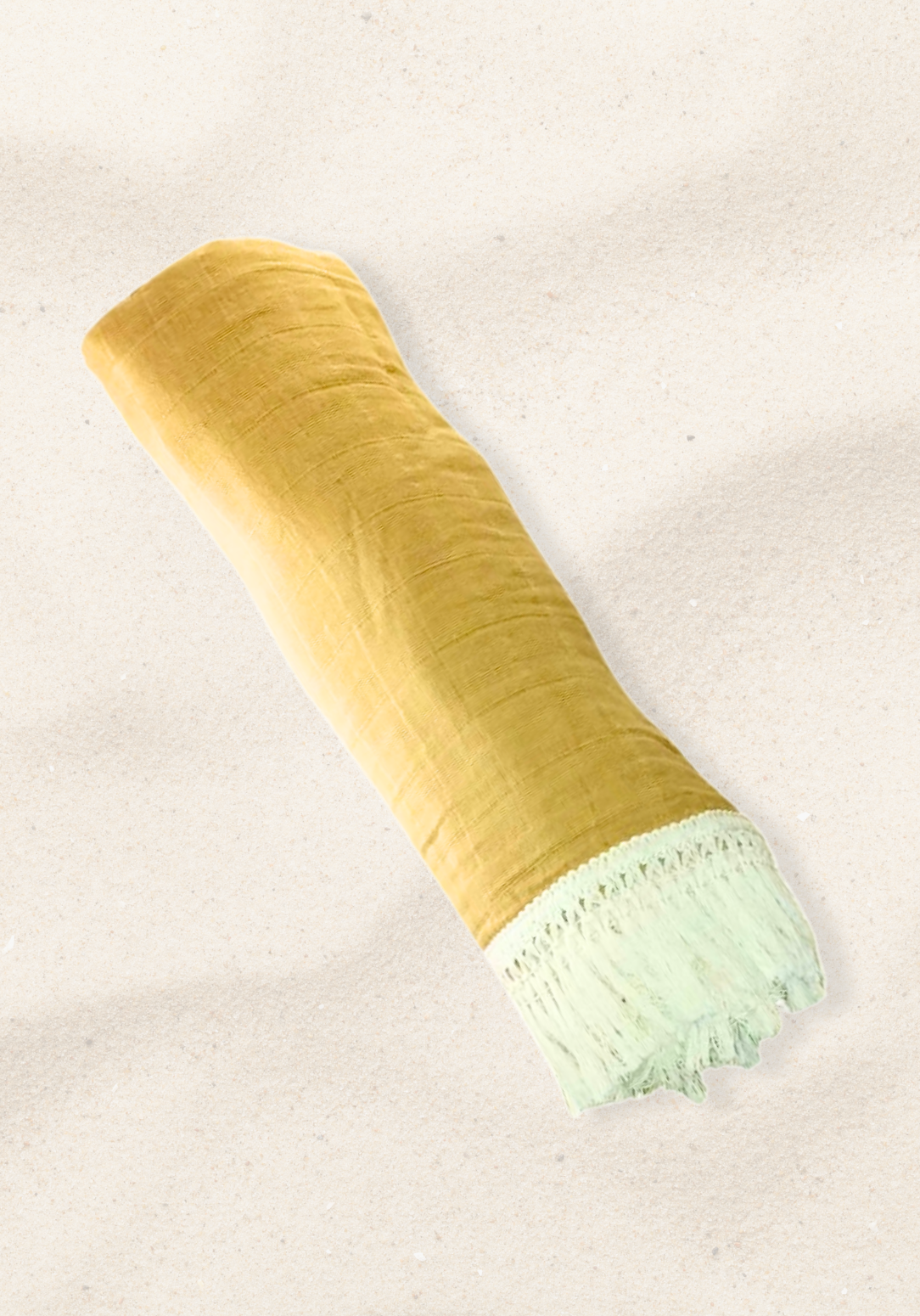 Rolled golden yellow cotton baby blanket with white fringed edges, displayed on a sand background.
