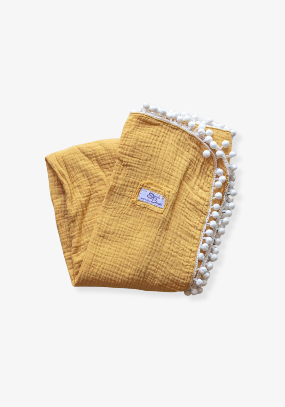 Mustard yellow organic cotton baby blanket with white pom-pom trim, folded neatly with a Bondi Booti label, placed on a neutral surface.