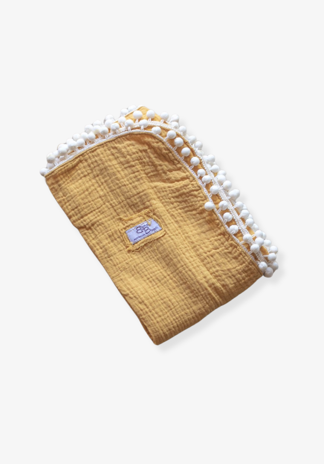 Mustard yellow organic cotton baby blanket with white pom-pom trim, folded neatly with a Bondi Booti label, placed on a neutral surface.