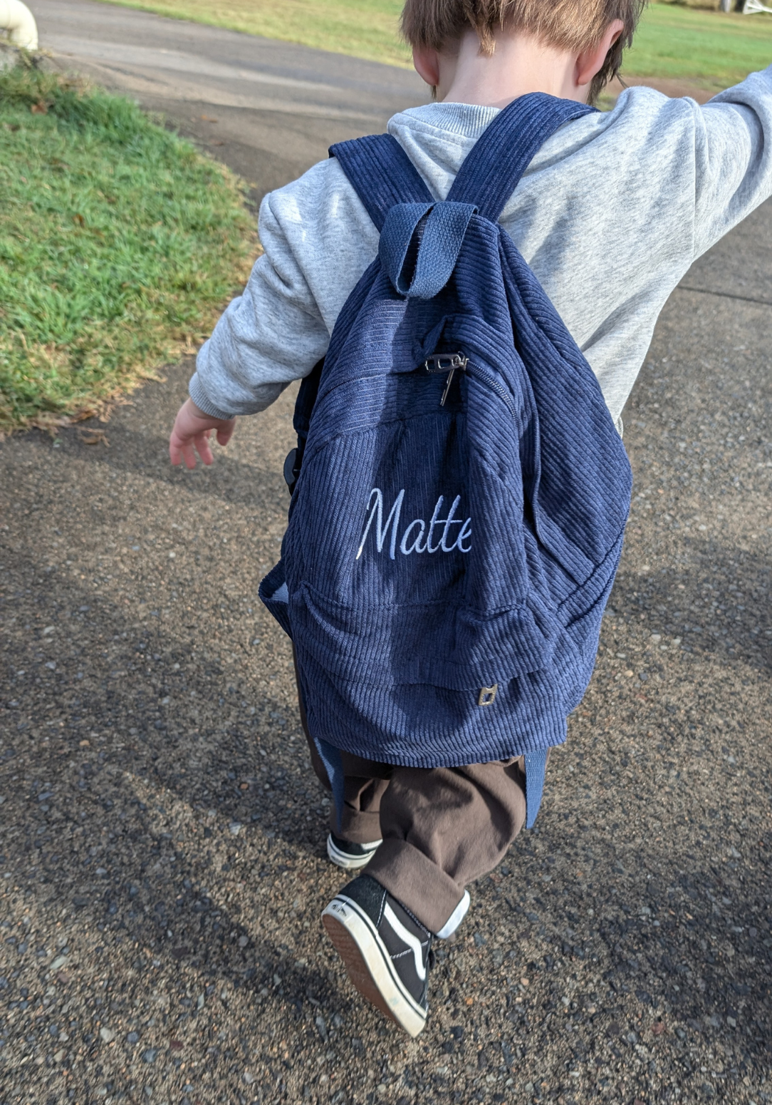Close-up of toddler wearing a navy blue personalized corduroy backpack with ‘Matteo’ embroidered, walking on footpath