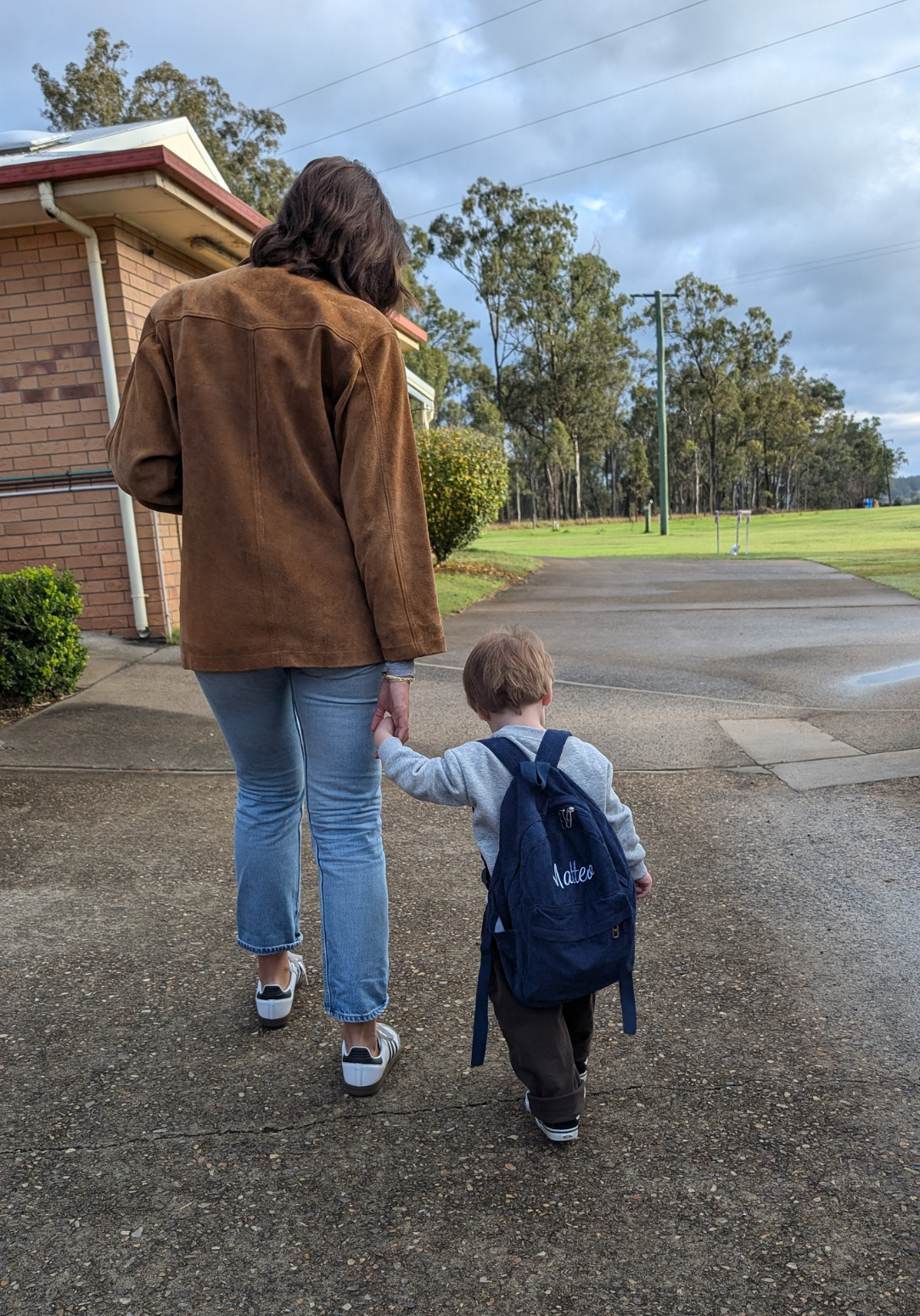 Toddler wearing a navy personalized backpack with ‘Matteo’ embroidery while walking outdoors holding hands with an adult